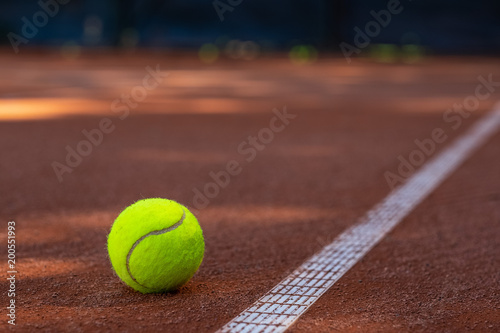 Closeup of one tennis ball close to a white line on a slug court with multiple balls blurred in the background