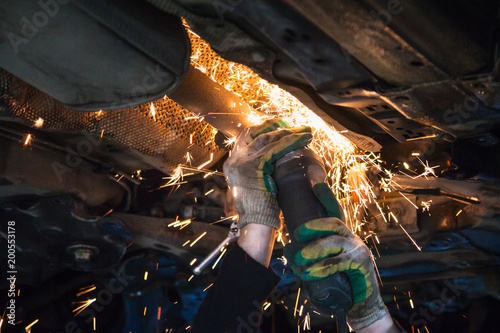 Fotografie mechanic cuts old muffler on car by angle grinder