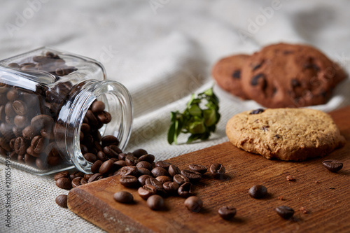Roasted coffee beans get out of overturned glass jar on homespun tablecloth, selective focus, side view photo