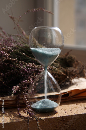 Time passing, sandglasses with blue sand, flowers, wood