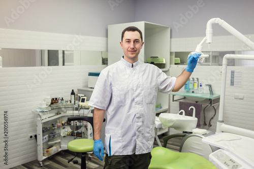 Male dentist standing over medical office background. Healthcare  profession  stomatology and medicine concept