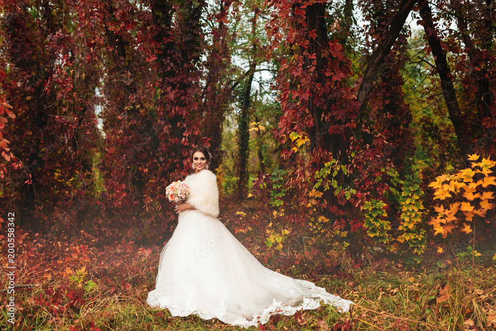 sensual bride stands in autumn forest and poses for camera