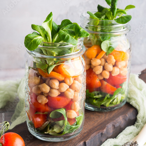 Fresh salad lunch with chickpeas, tomatoes, carrots and valerian served in mason jars