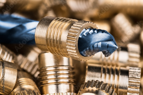 Threaded insert close-up and spiral flute tap. Beautiful detail of the cutting tool for threading with rays on tip and blurred background of bronze thread inserts. Idea of machining, build, metalwork.