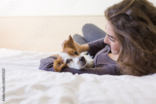 beautiful young woman lying on bed with her cute small dog besides. Home, indoors and lifestyle