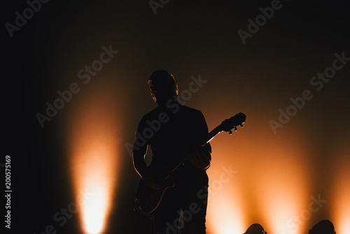 Rock band performs on stage. Guitarist plays solo. silhouette of guitar player in action on stage in front of concert crowd.