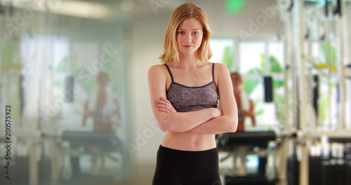 Caucasian woman in athletic clothing with arms crossed looking at camera in gym