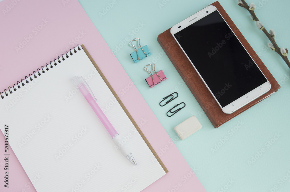 Concept for girl's desktop. On the desk is laptop, notepad for notes, phone, pen, pencil, paper clips, eraser, office supplies, spring tree twigs. The background is turquoise with white. Flat lay. Concept for girl's desktop. On the desk is laptop, notepad for notes, phone, pen, pencil, paper clips, eraser, office supplies, spring tree twigs. The background is turquoise with white. Flat lay.