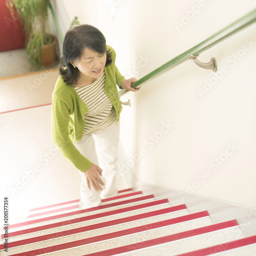 階段で膝を押さえるシニア女性