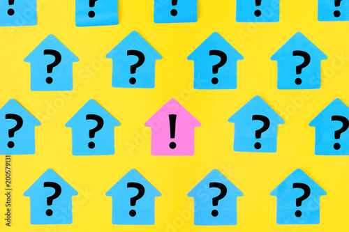Stickers in the form of houses on a bright yellow background. On blue sticky notes a question mark was written, in the center on a pink paper an exclamation mark.