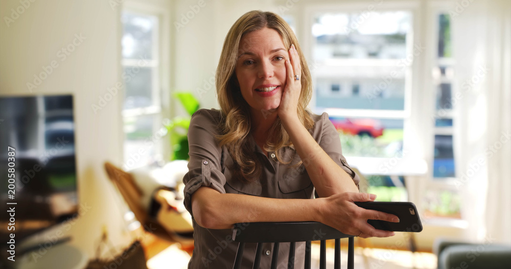 Caucasian woman with cellphone seated in living room talking to camera Caucasian woman with cellphone seated in living room talking to camera