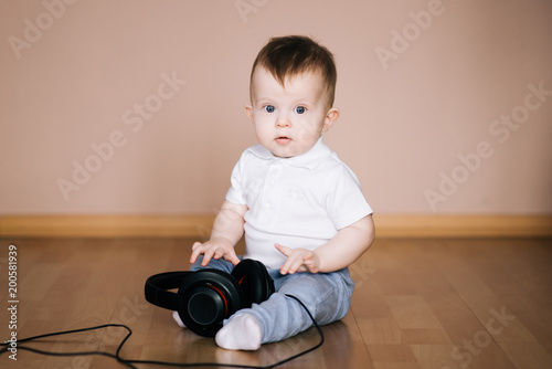 Cute young baby sitting on the floor at home playing with headphones listening to music