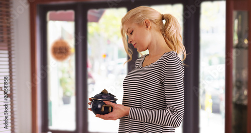 Caucasian woman looking at antique pot checking price tag inside store smiling