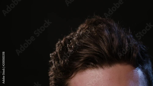 A young man touching his hair against a black background. Close-up macro shot