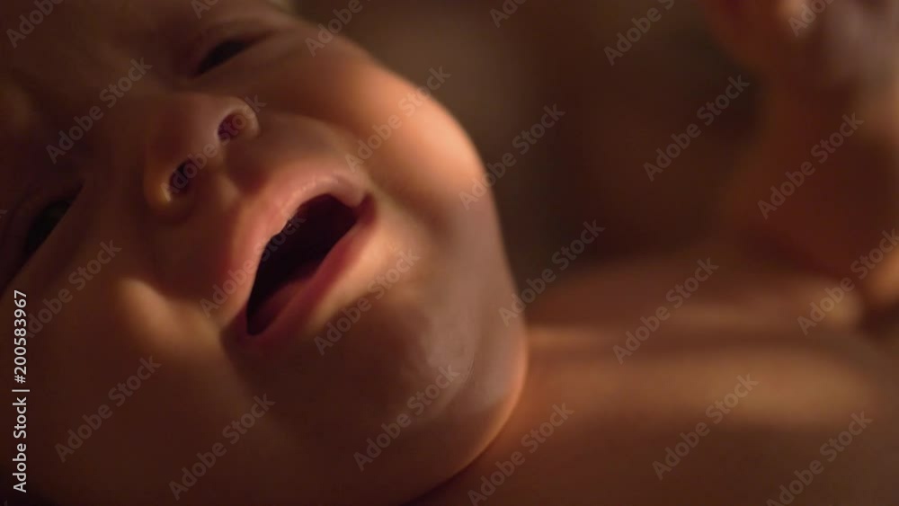 Slow motion close-up shot of three months baby crying. Indoor shot with sun light on the child face
