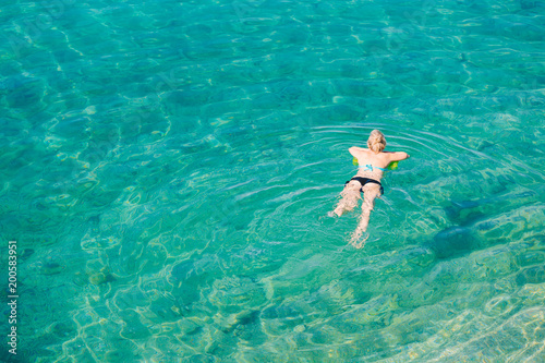 Aerial view of young blonde woman swimming in the transparent turquoise sea. Top view of slim lady relaxing on her holidays.