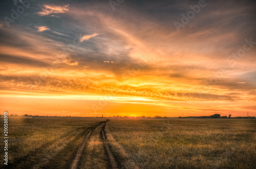Road in the steppe under amazing cloudy sunset sky
