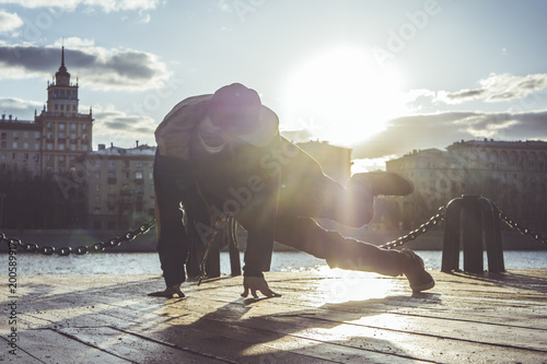 Murais de parede young man in snapback breakdancing in the city street during sunset