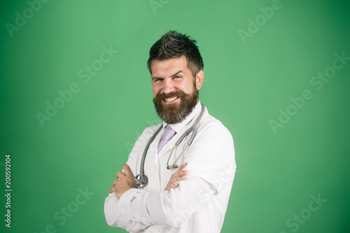 Doctor with beard and mustache, happy face, in white medical coat crossed hands. Successful bearded male physician with stethoscope in white uniform. Treatment, medicine and ambulance services concept