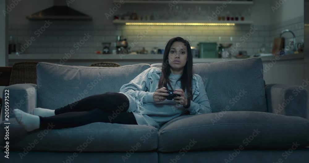 Teenage girl lying on the sofa playing a video game at night. Teenage girl lying on the sofa playing a video game at night.