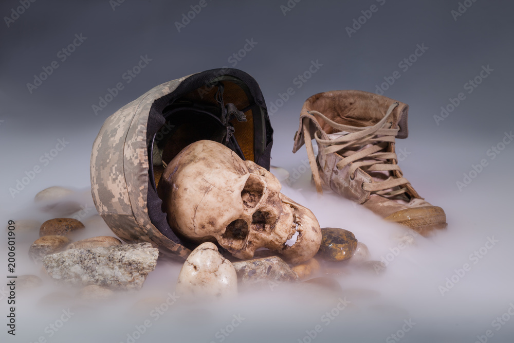 Corpses in military uniform on ice smoke. The human skull is next to the military cap and boots.