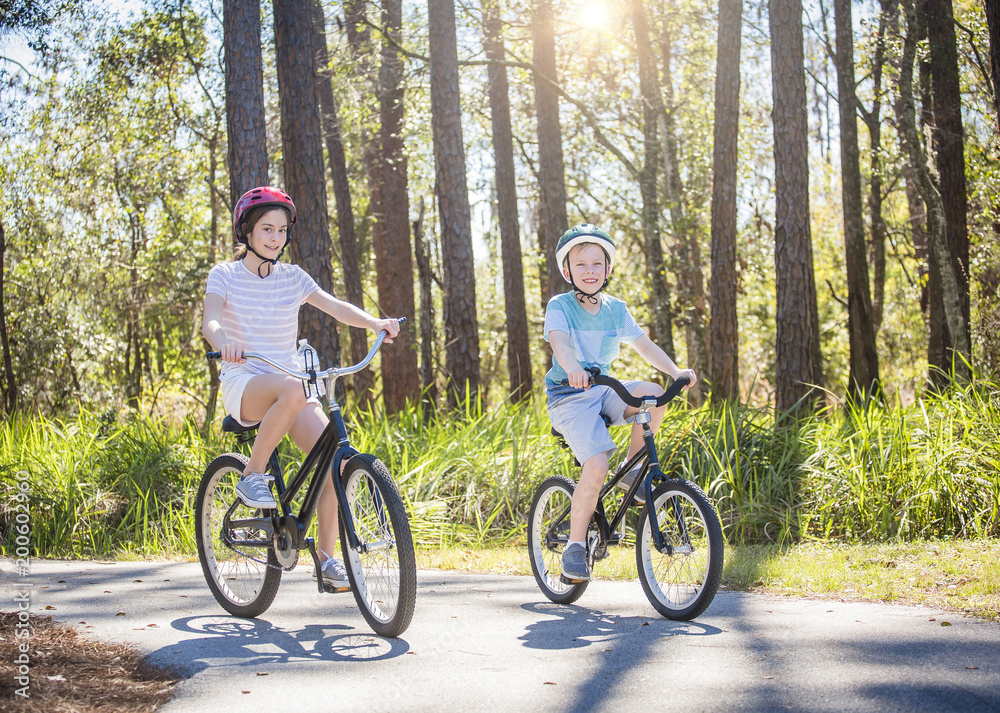 Two kids enjoying a fun bicycle ride together on a bike path in a green forest outdoors. Smiling and enjoying nature on a sunny warm day. Exercising and being active during the summer