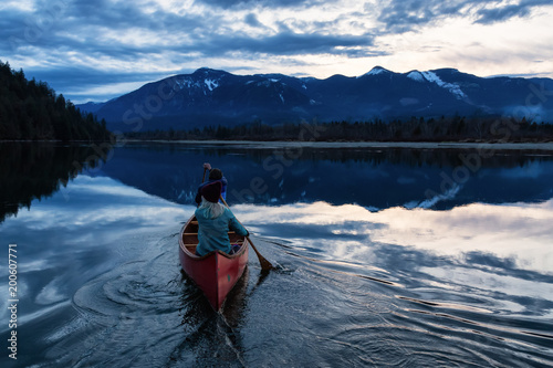 Adventurous people on a wooden canoe are enjoying the beautiful Canadian Mountain Landscape during a vibrant sunset. Taken in Harrison River, East of Vancouver, British Columbia, Canada. © edb3_16