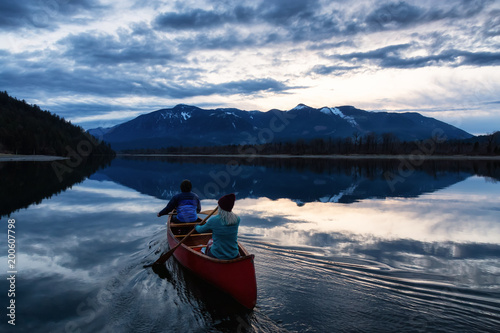 Adventurous people on a wooden canoe are enjoying the beautiful Canadian Mountain Landscape during a vibrant sunset. Taken in Harrison River, East of Vancouver, British Columbia, Canada.