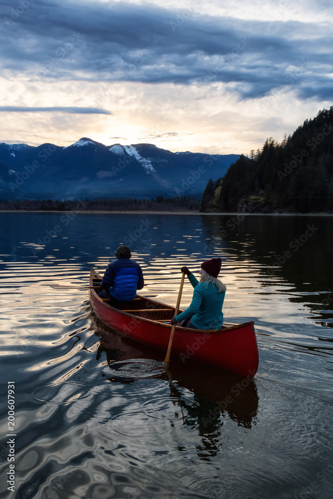 Adventurous people on a wooden canoe are enjoying the beautiful Canadian Mountain Landscape during a vibrant sunset. Taken in Harrison River, East of Vancouver, British Columbia, Canada.