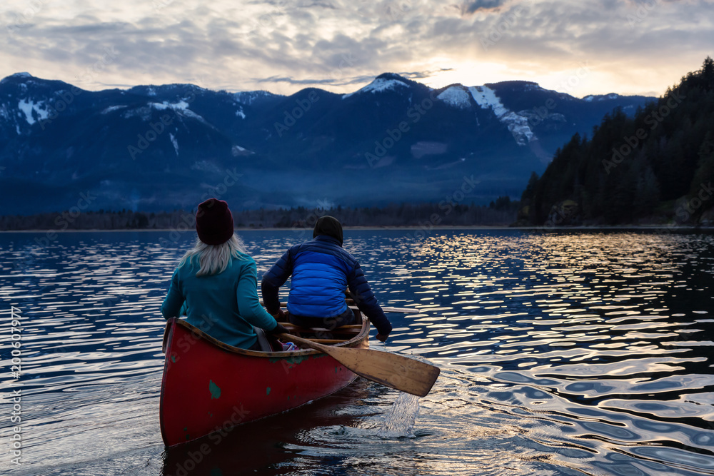 Adventurous people on a wooden canoe are enjoying the beautiful Canadian Mountain Landscape during a vibrant sunset. Taken in Harrison River, East of Vancouver, British Columbia, Canada.