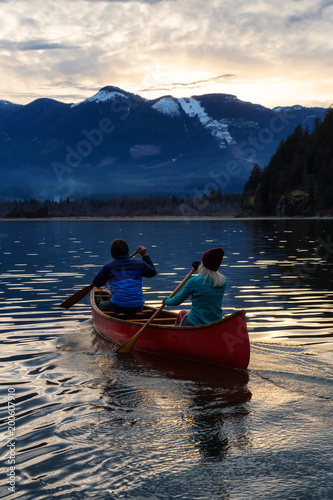 Adventurous people on a wooden canoe are enjoying the beautiful Canadian Mountain Landscape during a vibrant sunset. Taken in Harrison River, East of Vancouver, British Columbia, Canada.