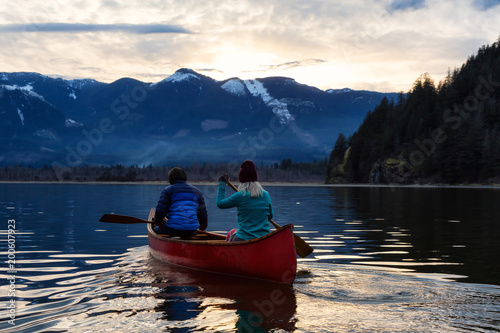 Adventurous people on a wooden canoe are enjoying the beautiful Canadian Mountain Landscape during a vibrant sunset. Taken in Harrison River, East of Vancouver, British Columbia, Canada.