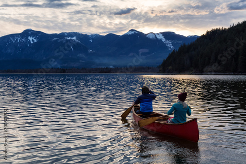 Adventurous people on a wooden canoe are enjoying the beautiful Canadian Mountain Landscape during a vibrant sunset. Taken in Harrison River, East of Vancouver, British Columbia, Canada. © edb3_16
