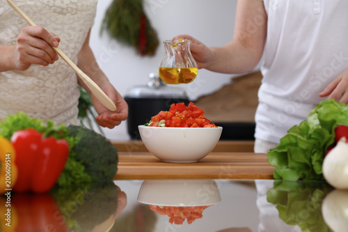 Closeup of human hands cooking in kitchen. Mother and daughter or two female friends mixing salad of vegetables. Healthy meal, vegetarian food and lifestyle concepts