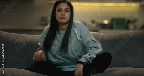 Woman sits down on a sofa, crosses her legs and turns the tv on using a remote control.
