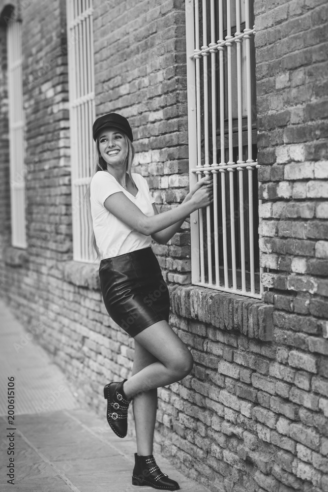 Young blonde woman wearing cap smiling near a brick wall.