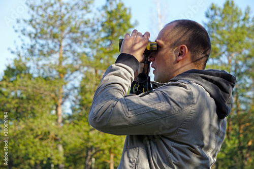 Young ornithologist looking through binoculars in the spring forest at the birds