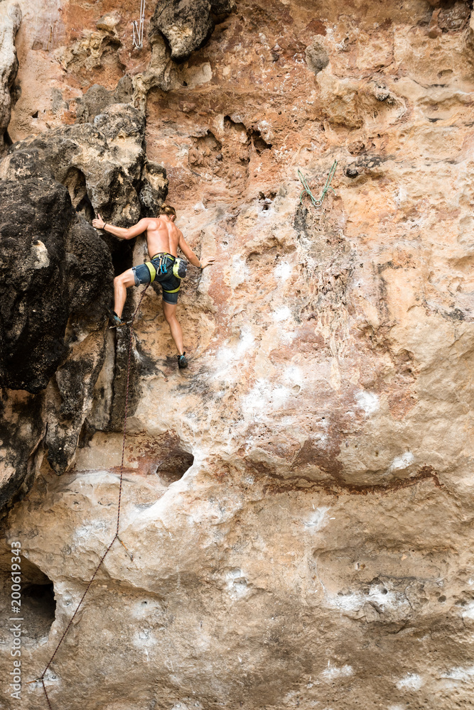 Young man climbing on a limestone cliff in Railay Beach Krabi, Thailand Young man climbing on a limestone cliff in Railay Beach Krabi, Thailand
