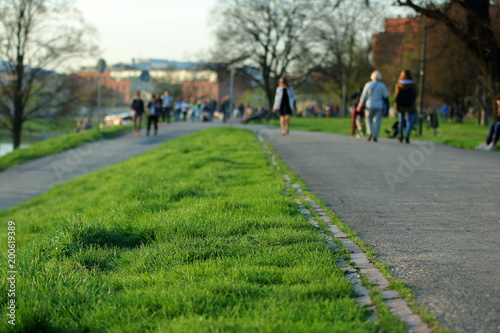Wallpaper Mural Bulwary nadwiślańskie w Krakowie, Polska, pas zielonej trawy, po wybetonowanych alejkach spacerują ludzie, rozmyci jak i drzewa, budowle Torontodigital.ca
