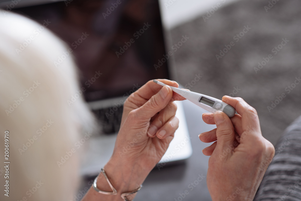 Selective focus of a thermometer in hands of a nice senior woman Selective focus of a thermometer in hands of a nice senior woman
