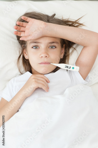 sick girl lying in bed with a thermometer in mouth. Top view
