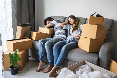 Young tried couple moving in new home, sitting and relaxing on sofa with cardboard boxes