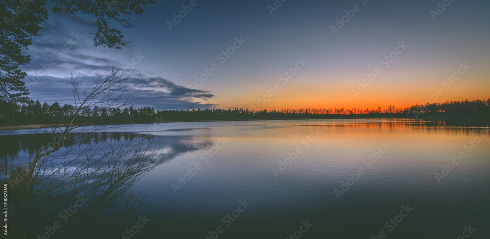 Colorful sunset over the lake in late evening in Spring. Peaceful scenery with clear sky and reflections in water.
