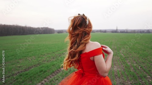 young woman in a luxurious red dress standing in a field looking at the camera and smiling, close-up photo