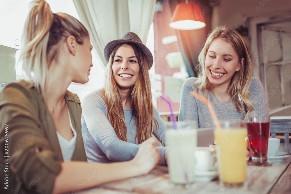 Female friends enjoying in conversation and drinking coffee in cafe and using digital tablet.