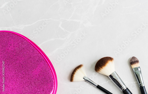 3 black cosmetic brushes and a bright pink cosmetic bag on a marble surface  with copy space.