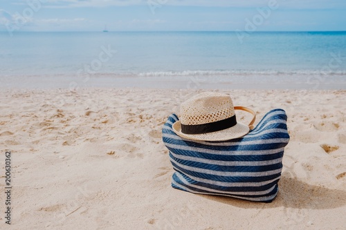 Blue beach bag with hat on the sandy beach with the blue sky background