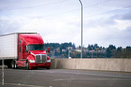 Red modern big rig semi truck tractor transporting commercial goods in refrigerator semi trailer on wide highway photo
