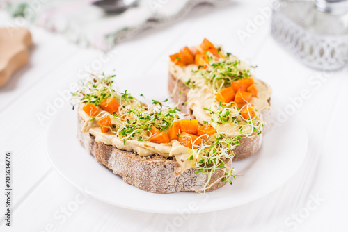 Healthy sandwiches for breakfast with humus, baked carrot and microgreen sprouts on the served white wooden table. Healthy food, vegitarian diet concept. Selective focus, space for text.