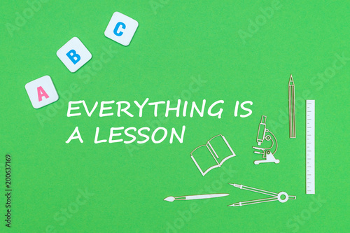 text everyting is a lesson, from above wooden minitures school supplies and abc letters on green background photo